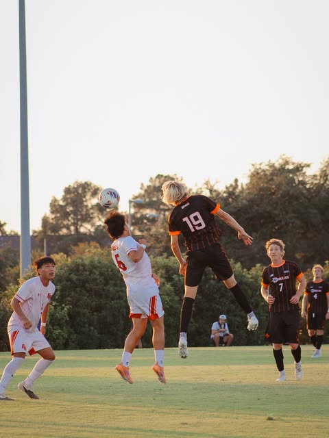 Soccer players competing for a header at sunset